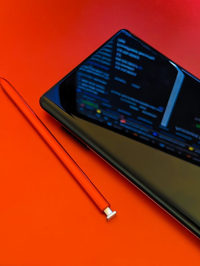 our-story Close-up of a smartphone with a stylus on a bright red surface, showcasing modern technology.
